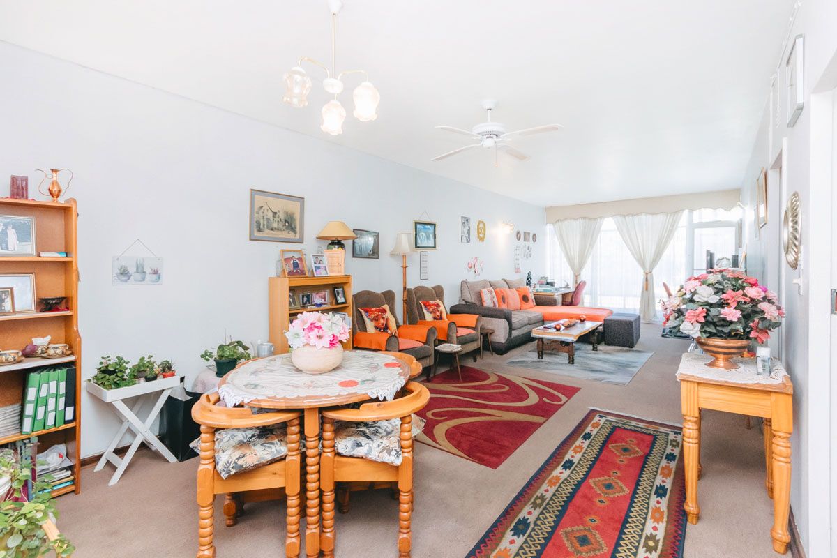 A spacious living room featuring carpeted flooring, a ceiling fan, and a central chandelier, offering a comfortable and functional layout.