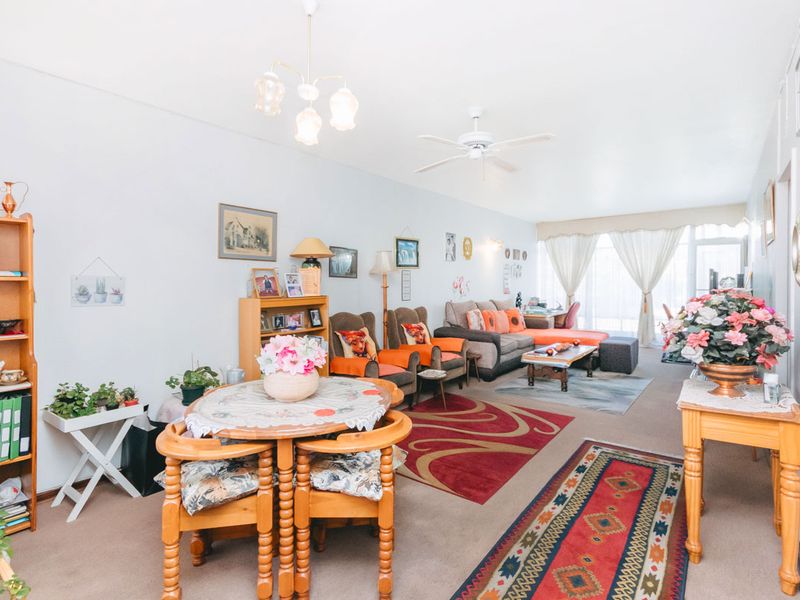 A spacious living room featuring carpeted flooring, a ceiling fan, and a central chandelier, offering a comfortable and functional layout.