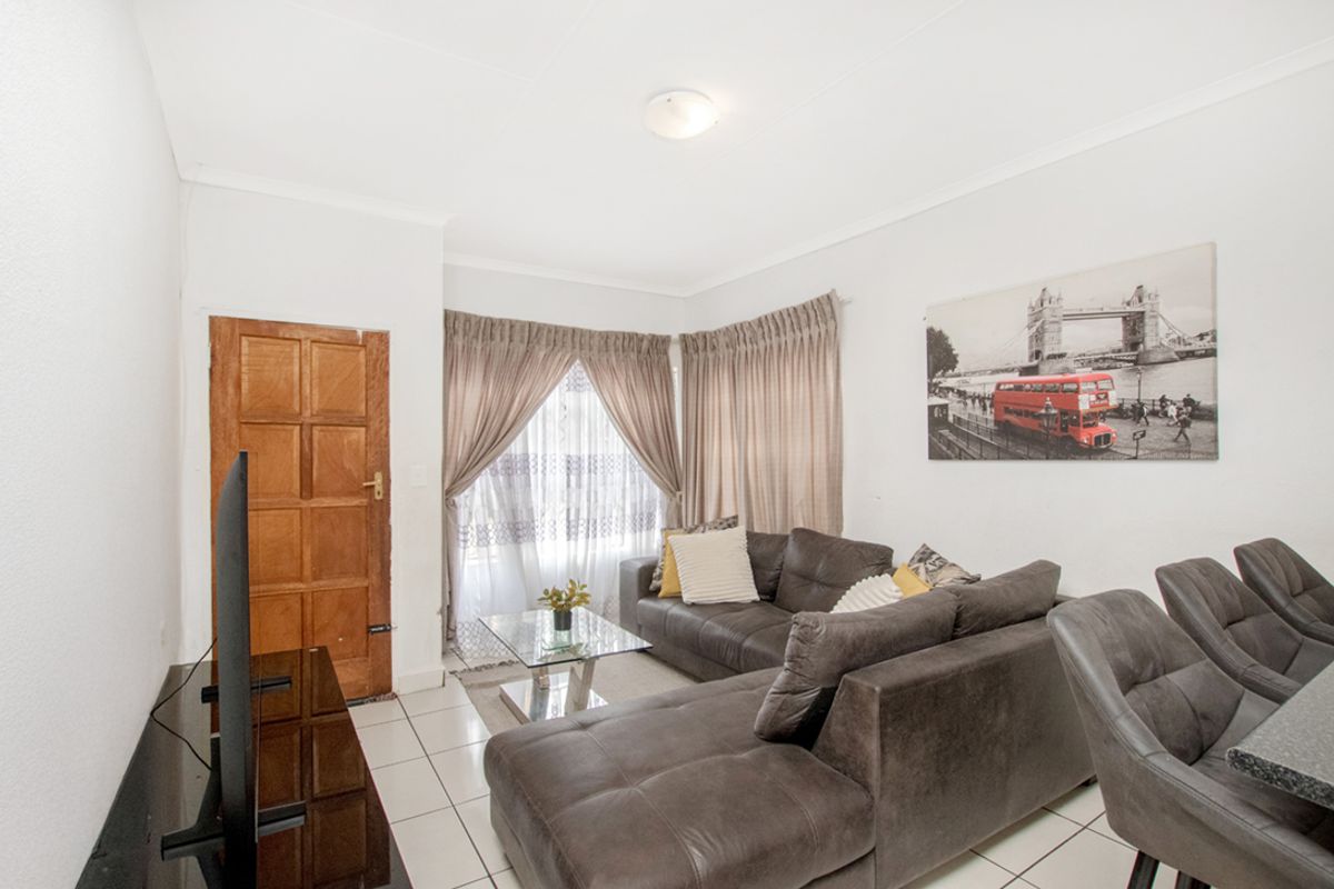 A bright living room featuring tiled flooring, a timber panel door, and large windows with curtain tracks, offering a functional and neutral living space.