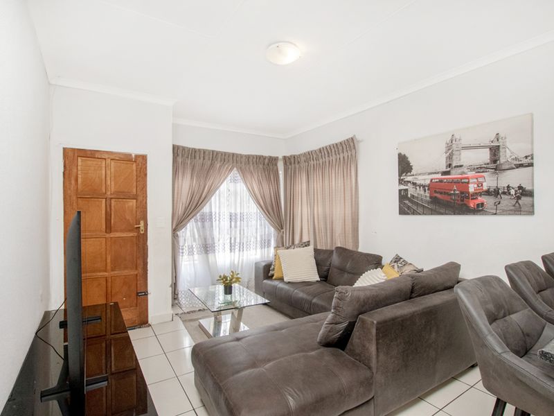 A bright living room featuring tiled flooring, a timber panel door, and large windows with curtain tracks, offering a functional and neutral living space.