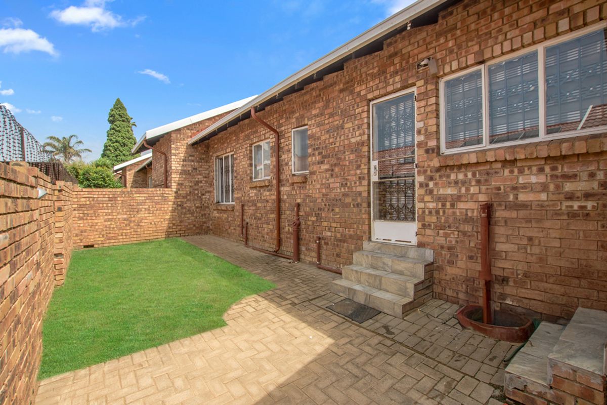 Rear exterior view of the townhouse featuring a face brick facade, paved patio area, and a small private garden space.
