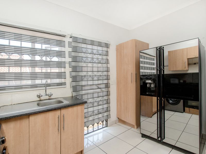 A functional scullery area featuring laminate cabinetry, a stainless steel sink, and tiled flooring, providing additional workspace and storage adjacent to the main kitchen.