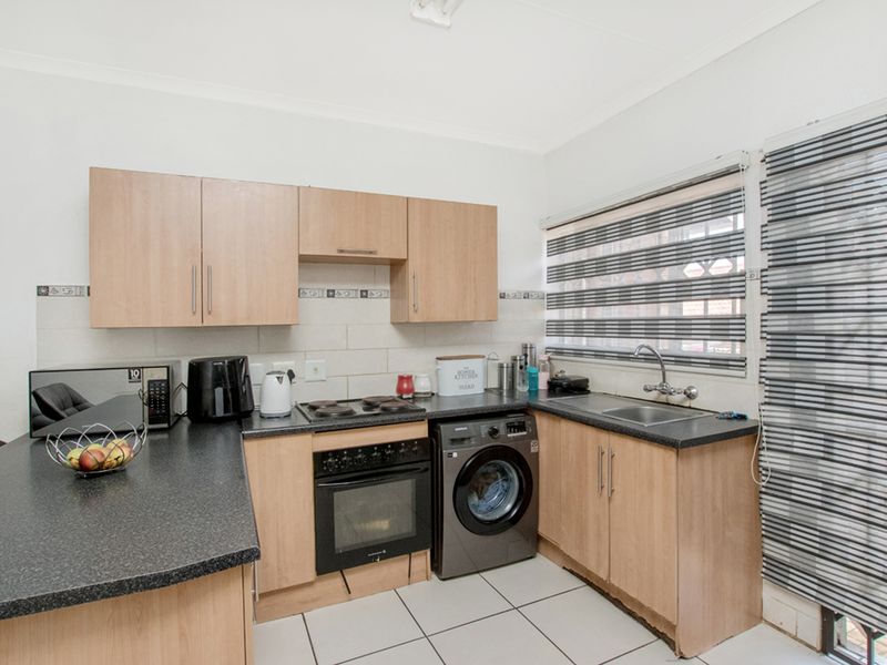 Functional kitchen featuring laminate cabinetry, dark countertops, built-in oven, electric hob, and tiled flooring with a convenient integrated laundry space.