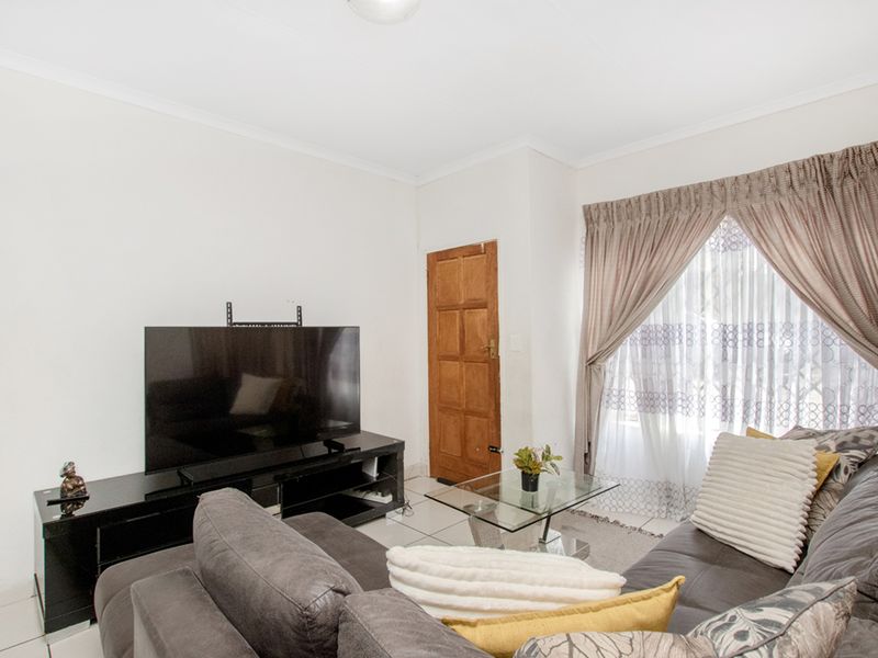 A living room featuring tiled flooring and a wooden door, providing a functional and neutral space for relaxation.