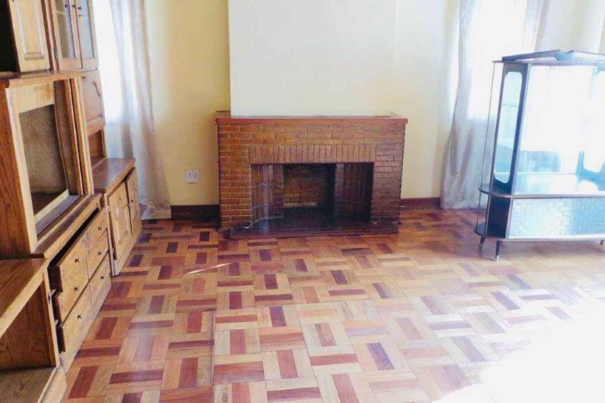 A living room featuring a classic brick fireplace and traditional parquet flooring, offering a solid foundation for a modern interior update.