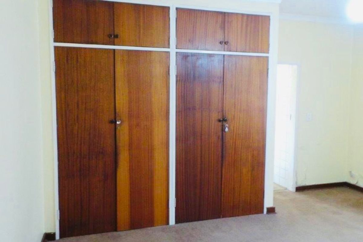 A vacant bedroom featuring floor-to-ceiling wooden built-in cupboards and carpeted flooring, requiring some cosmetic updates to the walls and finishes.