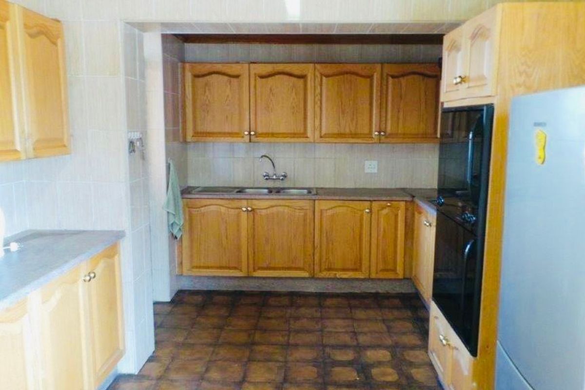 A functional kitchen featuring traditional wooden cabinetry, laminate countertops, a double basin sink, and a built-in oven with tiled finishes throughout.