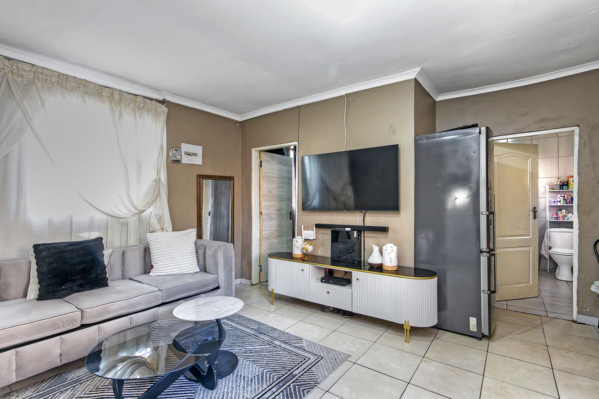 A living room area featuring tiled flooring and coved ceilings, showing signs of wear on the wall finishes and door frames.