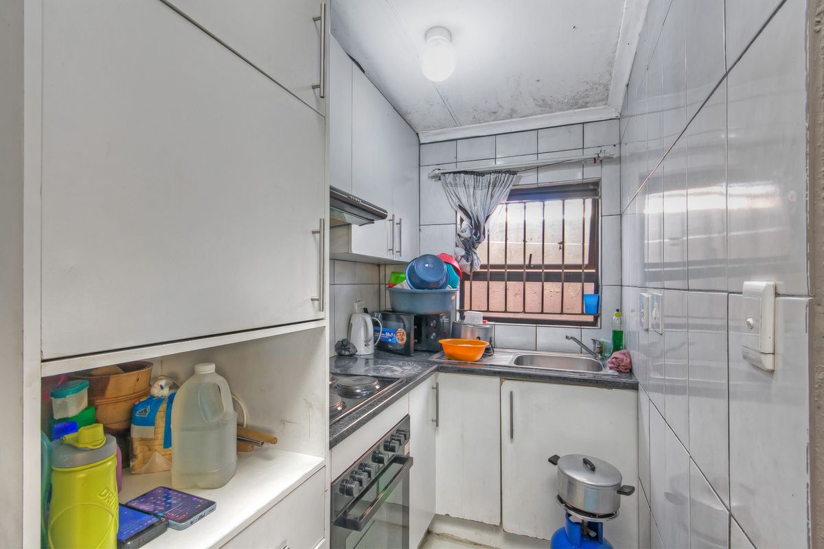 Compact kitchen featuring built-in cabinetry, a stainless steel sink, and integrated cooking appliances, requiring maintenance and cosmetic updates to improve the space.