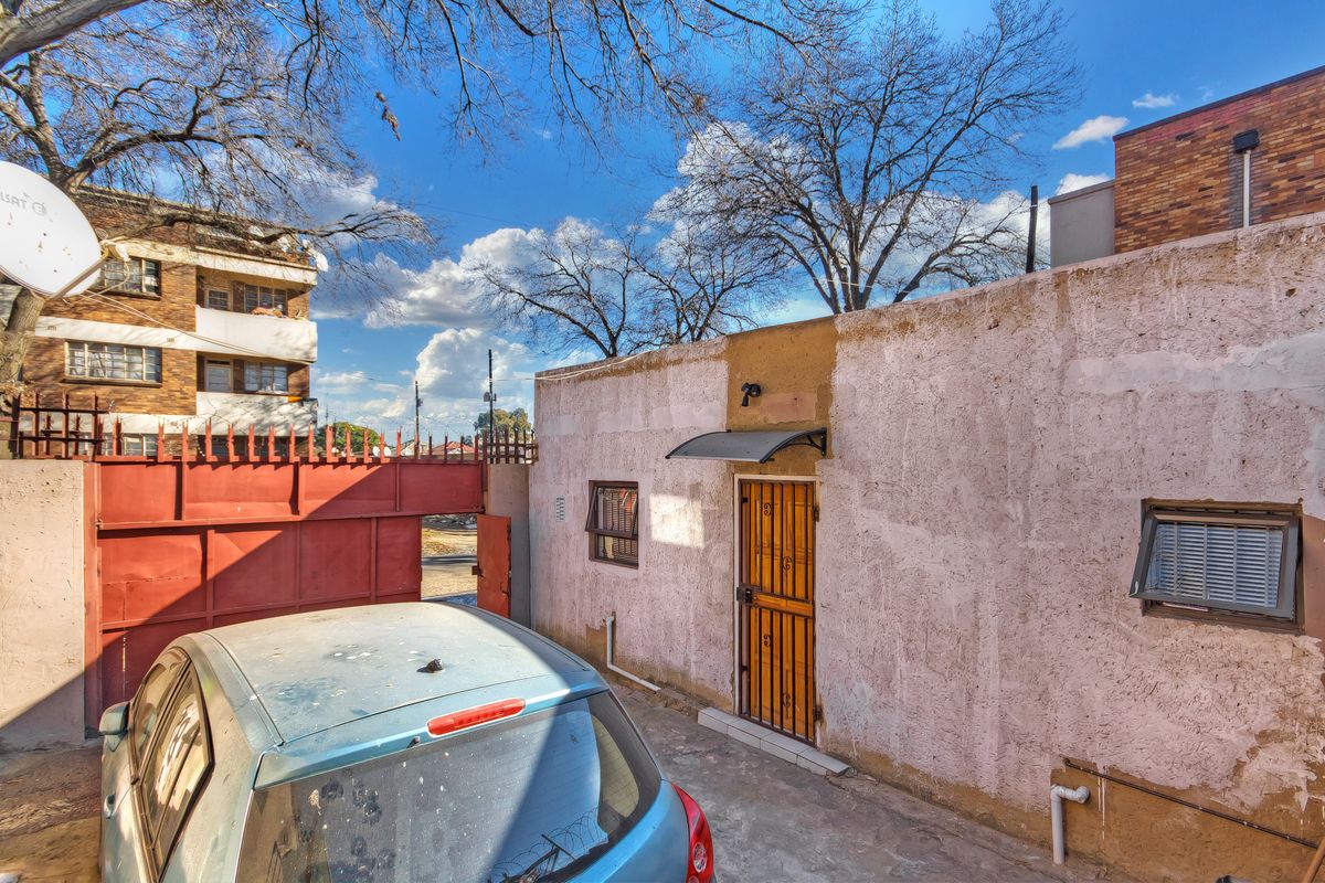 Rear exterior view of the townhouse featuring a security gate, awning, and weathered wall finishes requiring maintenance.