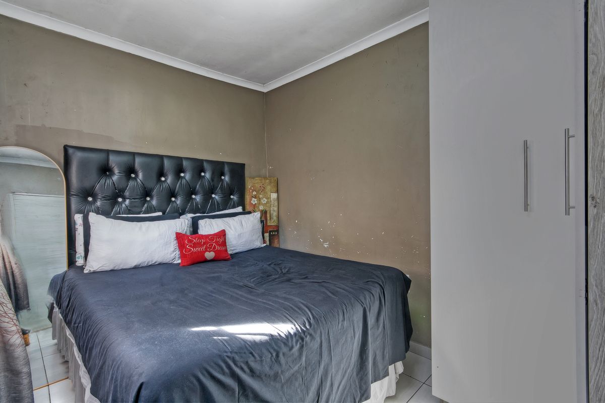 A bedroom featuring tiled flooring, a built-in wardrobe, and coving, currently showing signs of wear on the wall surfaces.