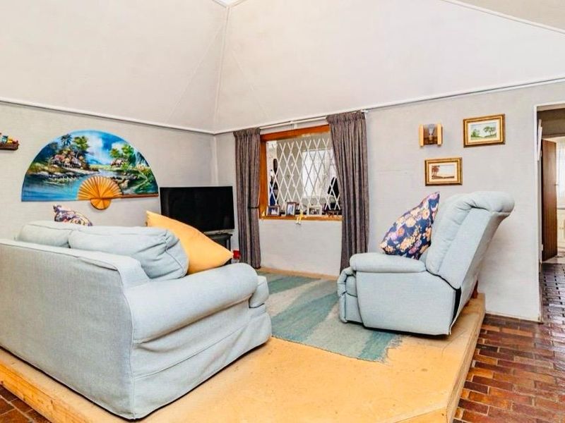 Living room featuring a vaulted ceiling, brick flooring, and a raised timber platform area with a diamond-pattern security window grille.