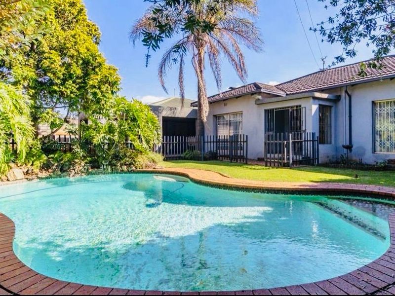 A private backyard featuring a swimming pool with brick coping, surrounded by a landscaped garden and a rear view of the house.