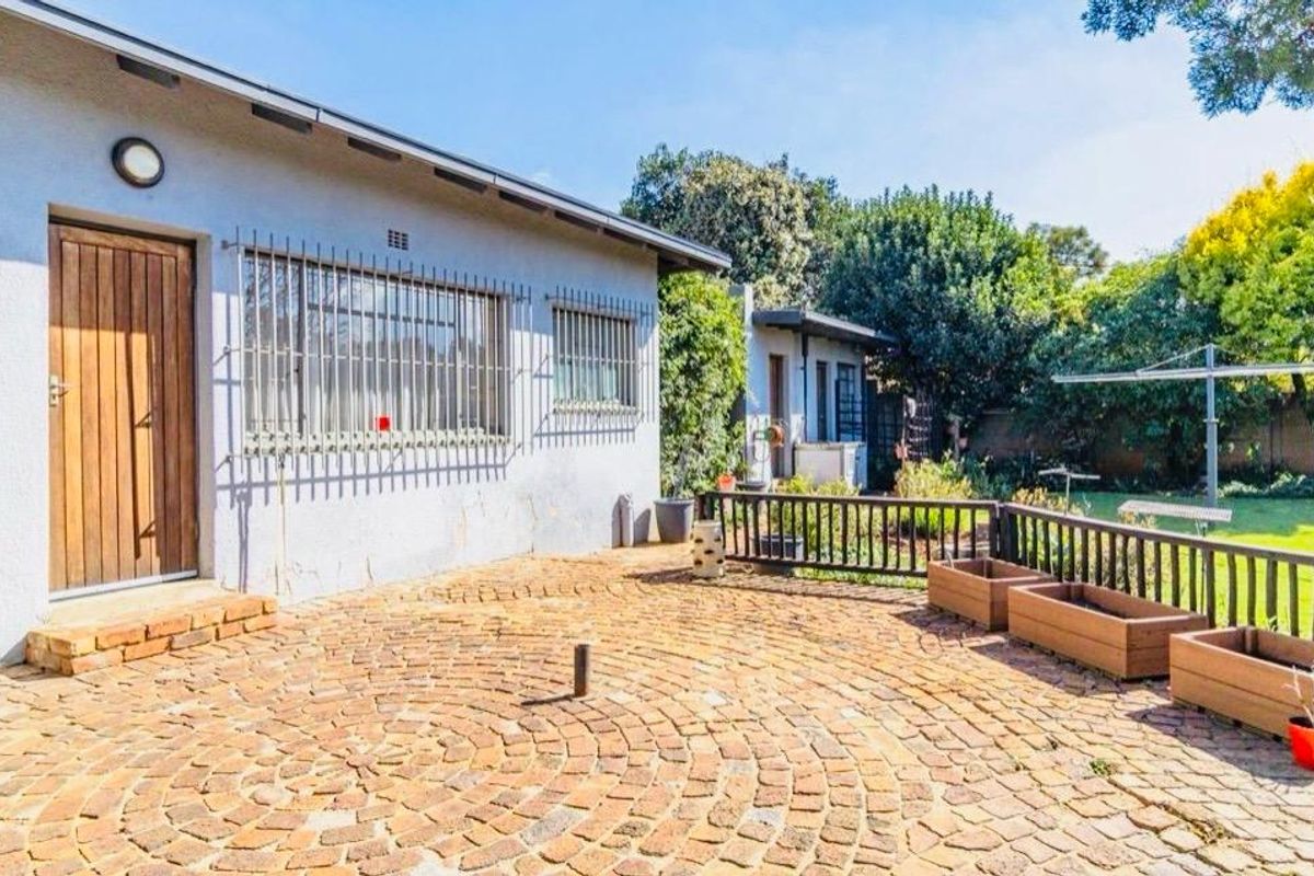 Rear exterior view featuring a circular brick paved patio, security-fitted windows, and a well-maintained garden area.