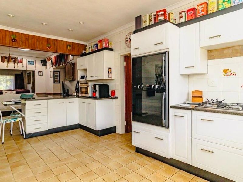 Open-plan kitchen featuring white cabinetry, built-in oven, gas hob, and tiled flooring, seamlessly flowing into the adjacent living area.