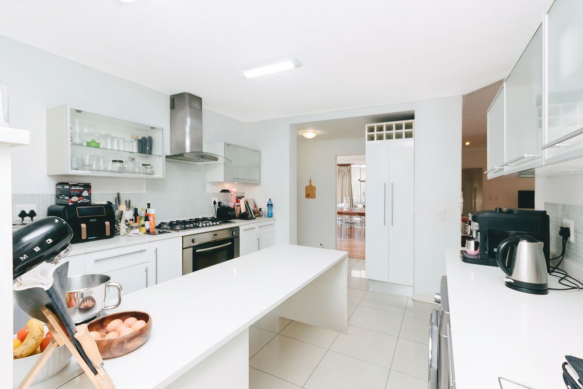 Modern kitchen featuring white cabinetry, stone countertops, a gas hob, built-in oven, and stainless steel extractor fan with tiled flooring.