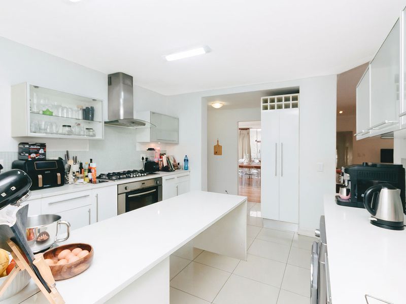 Modern kitchen featuring white cabinetry, stone countertops, a gas hob, built-in oven, and stainless steel extractor fan with tiled flooring.