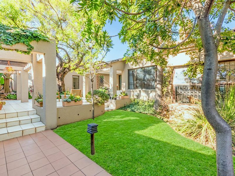 A well-maintained rear garden featuring a tiled patio area, pergola structure, and established trees, providing a pleasant outdoor living space.