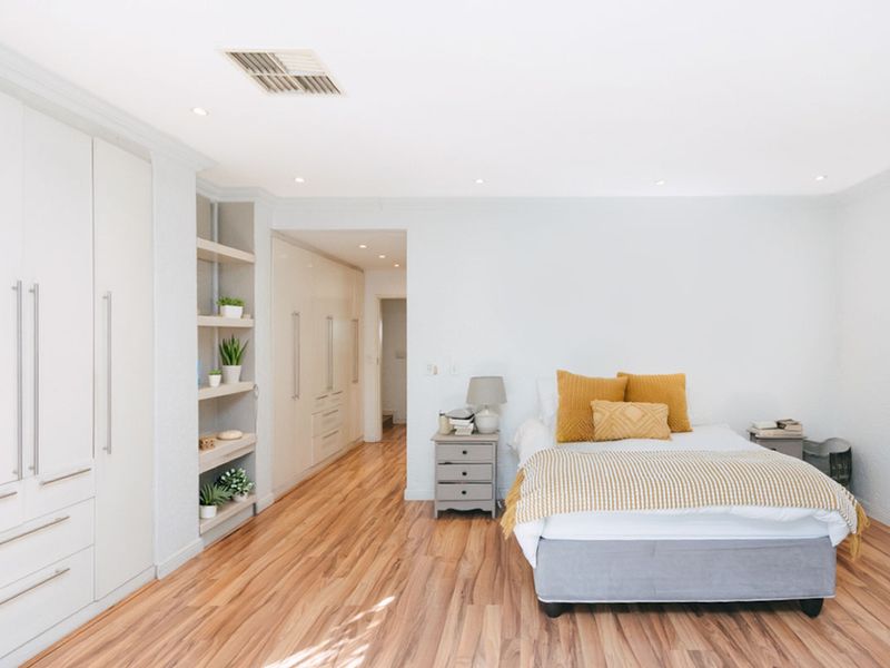 A bright, well-maintained bedroom featuring extensive built-in cabinetry, recessed shelving, and modern laminate flooring with integrated downlighting.