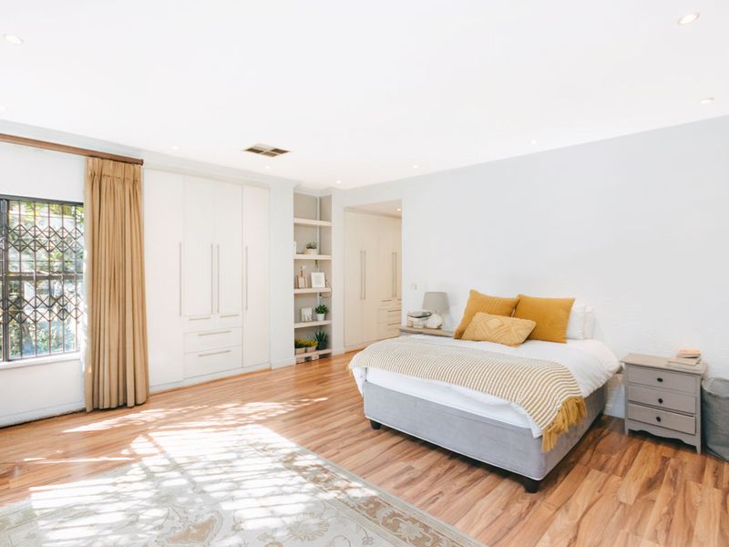 Spacious bedroom featuring light laminate flooring, extensive built-in cabinetry, recessed shelving, and large windows with security bars.