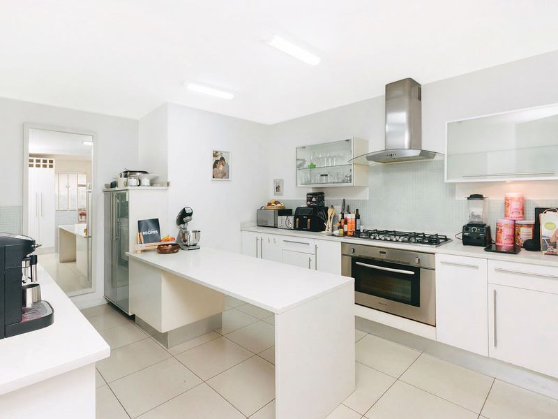 Modern kitchen featuring white cabinetry, a gas hob, built-in oven, stainless steel extractor fan, and a functional peninsula counter with tiled flooring.