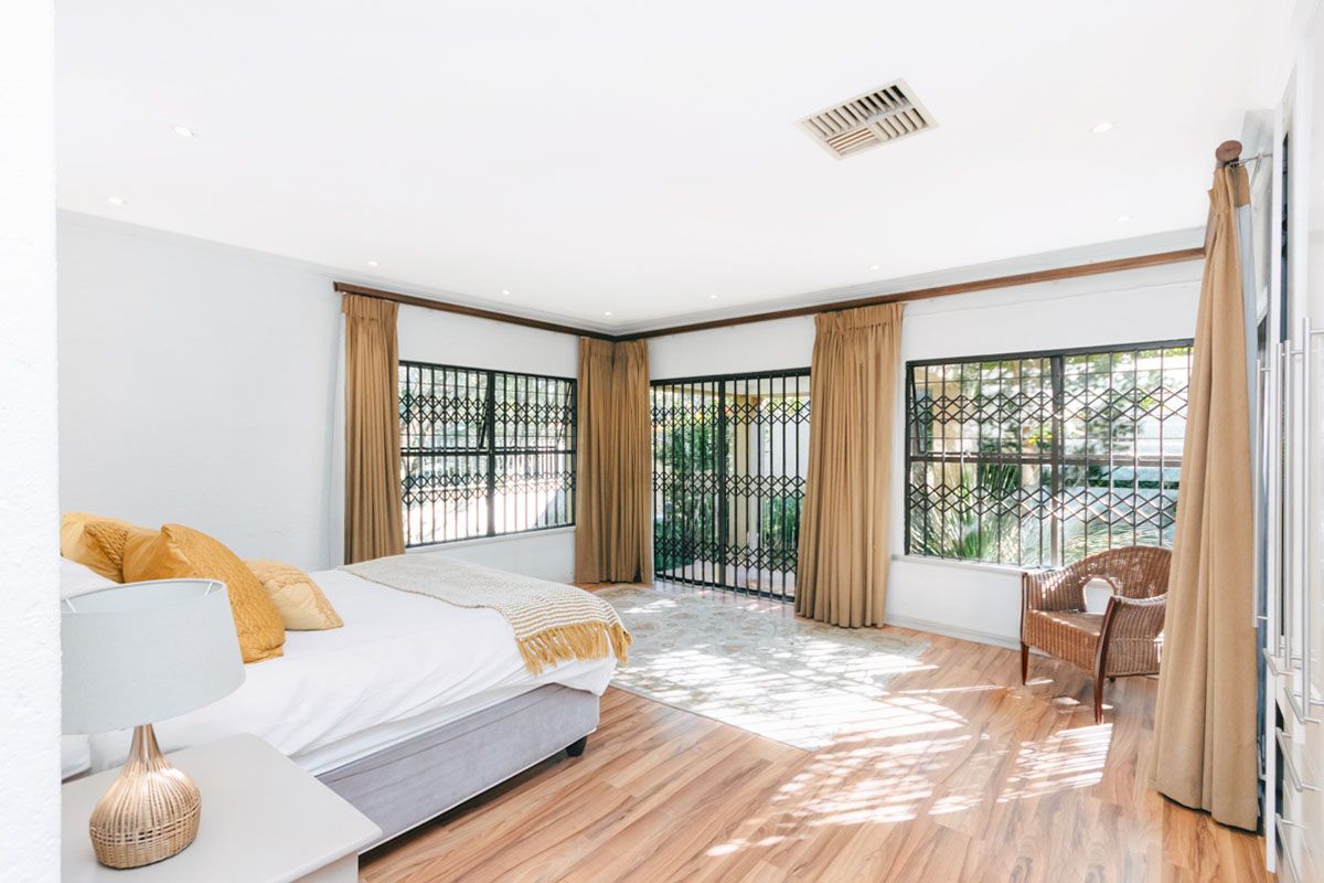 Spacious bedroom featuring laminate flooring, recessed lighting, and large windows with security gates, offering direct access to the outdoor area.