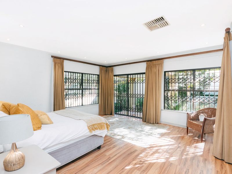 Spacious bedroom featuring laminate flooring, recessed lighting, and large windows with security gates, offering direct access to the outdoor area.