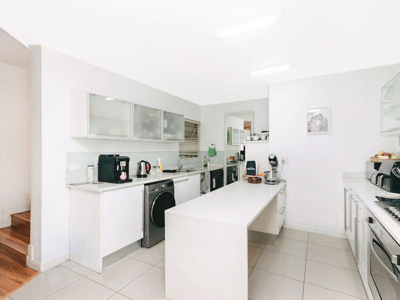 Modern kitchen featuring white cabinetry, stone countertops, integrated oven, gas hob, and tiled flooring with an adjacent laundry area.