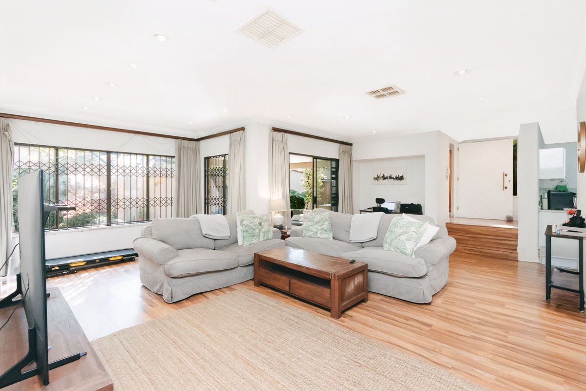 Spacious living room featuring laminate flooring, recessed downlighting, and large windows with security gates, providing access to the outdoor area.