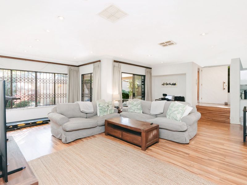 Spacious living room featuring laminate flooring, recessed downlighting, and large windows with security gates, providing access to the outdoor area.