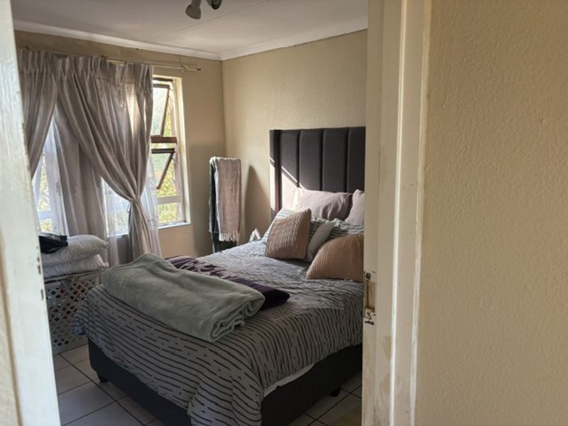 A standard bedroom featuring tiled flooring and an aluminium window frame, presenting a functional space with potential for cosmetic updates.