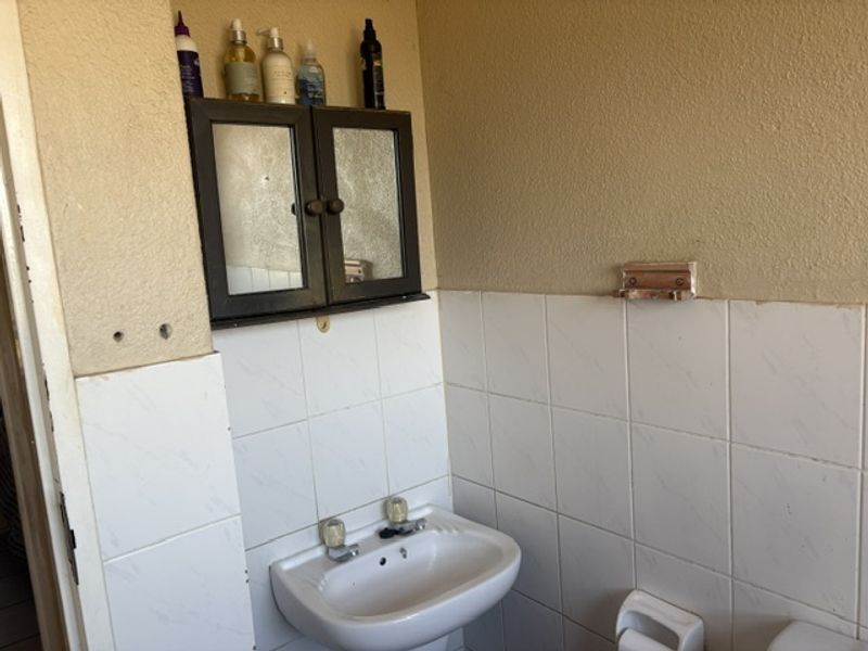 A functional bathroom featuring a pedestal basin, wall-mounted medicine cabinet, and partial wall tiling, currently showing signs of wear and minor wall damage.