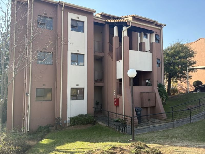 Rear elevation of a multi-story townhouse complex featuring balconies, external staircases, and established communal garden areas.