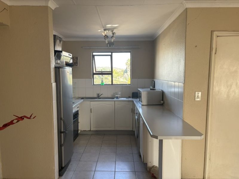 A functional kitchen featuring built-in cabinetry, a tiled backsplash, and a breakfast bar, offering a practical layout with potential for cosmetic updates.