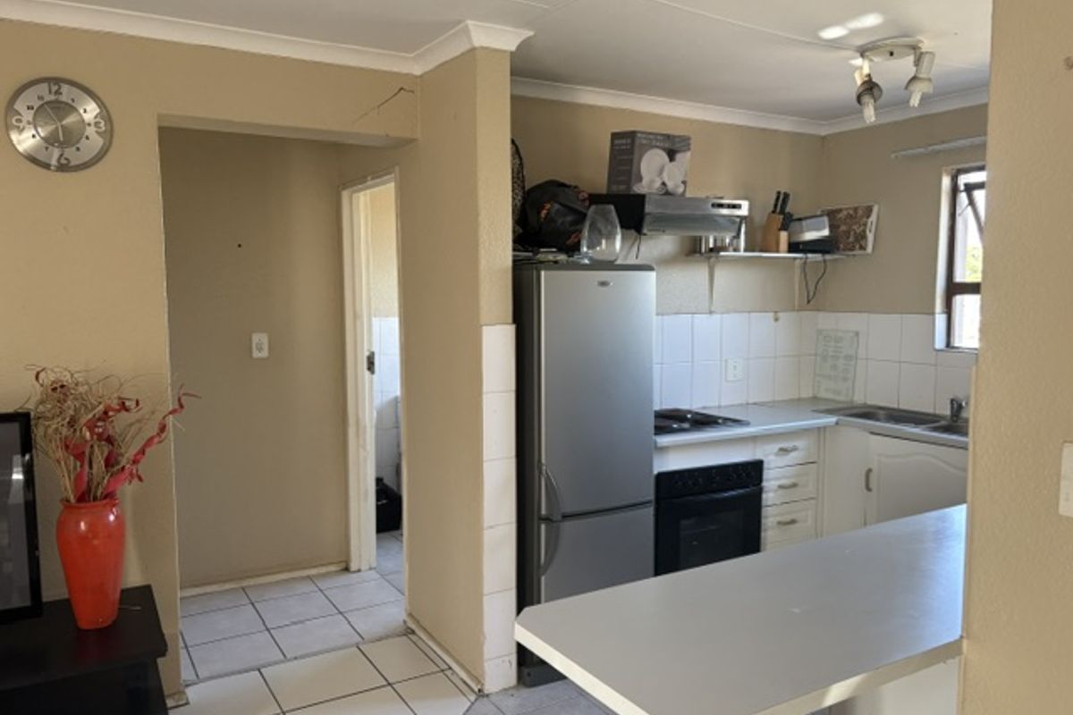 A functional kitchen featuring built-in cabinetry, a breakfast bar, and tiled splashbacks, requiring some cosmetic updates to the wall finishes.