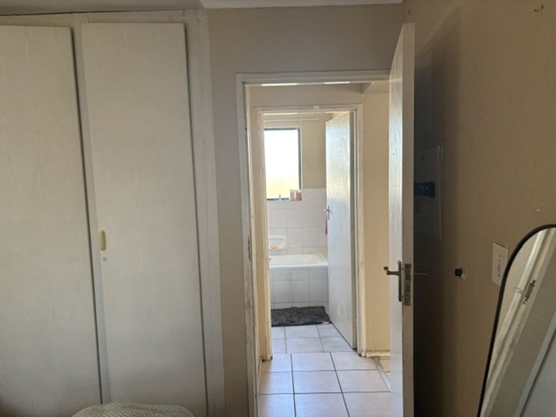 A bedroom featuring built-in cupboards and tiled flooring, with a direct view into an adjacent bathroom.