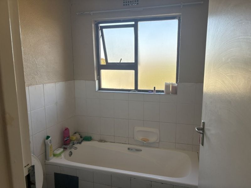 A functional bathroom featuring a standard bathtub with tiled splashback and a window, offering a blank canvas for potential renovation and modernization.