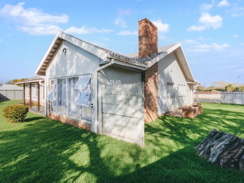 Rear view of the house featuring a brick chimney, tiled roof, and a spacious lawn area with a concrete boundary wall.