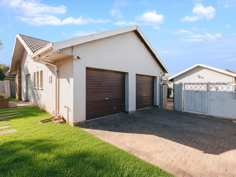 Exterior view of a double garage with brown roller doors, paved driveway, and adjacent gated access to the property.
