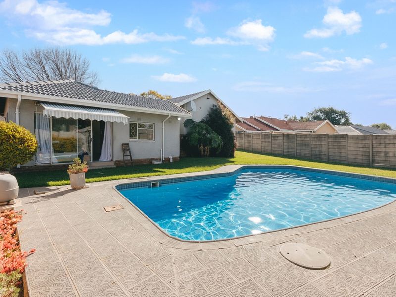 Rear view of the property featuring a swimming pool, paved patio area, retractable awning, and a well-maintained garden with boundary walling.