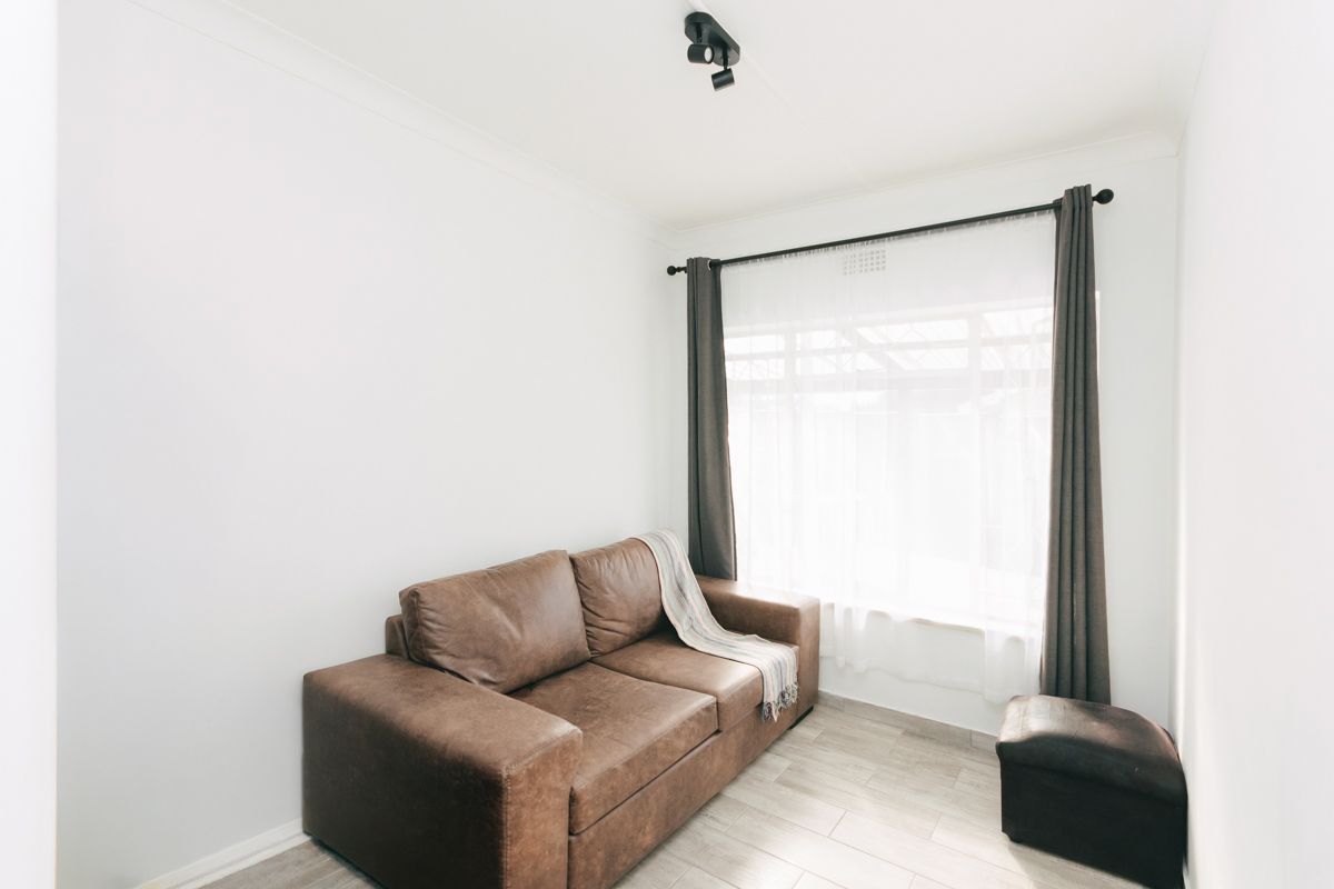 A bright living room featuring neutral tiled flooring, clean white walls, and a large window with installed curtain rods and lighting fixtures.