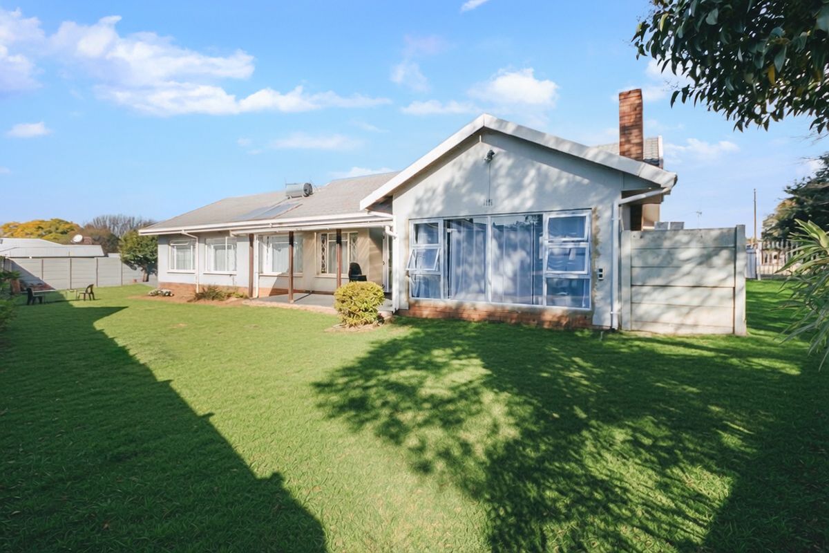 Rear view of the house featuring a spacious lawn, covered patio, brick chimney, and solar water heating system installed on the tiled roof.