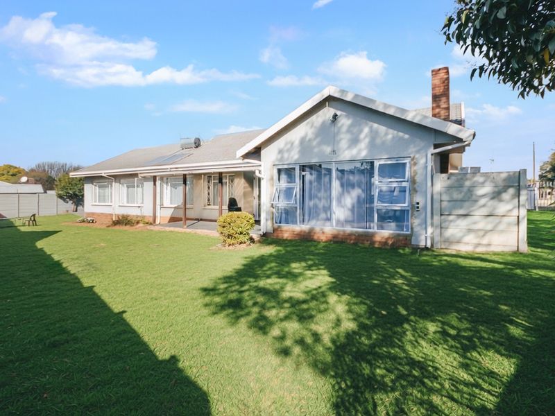 Rear view of the house featuring a spacious lawn, covered patio, brick chimney, and solar water heating system installed on the tiled roof.