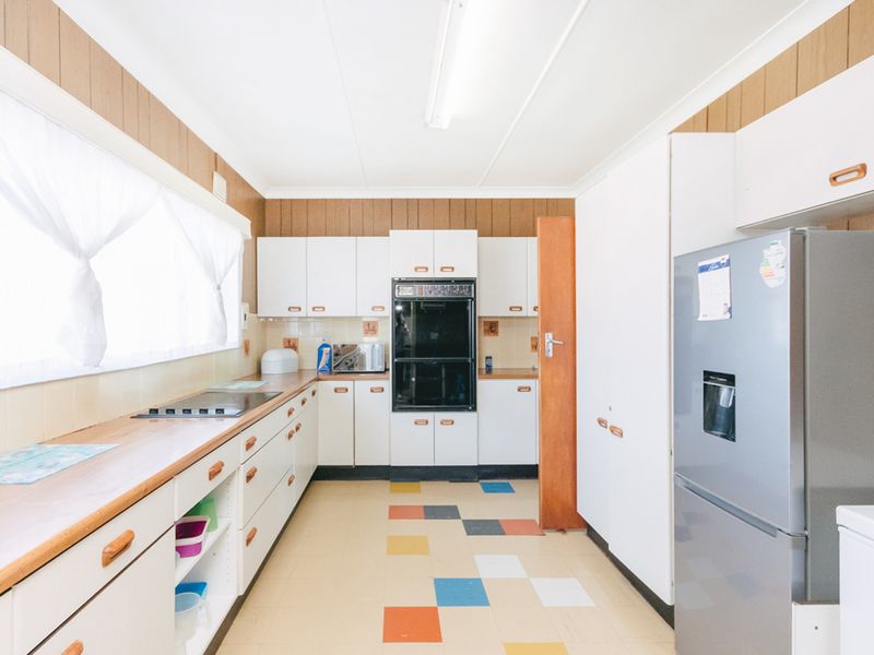 A dated kitchen featuring white cabinetry, built-in oven, cooktop, and laminate countertops with wood-look wall paneling and multi-colored vinyl flooring.