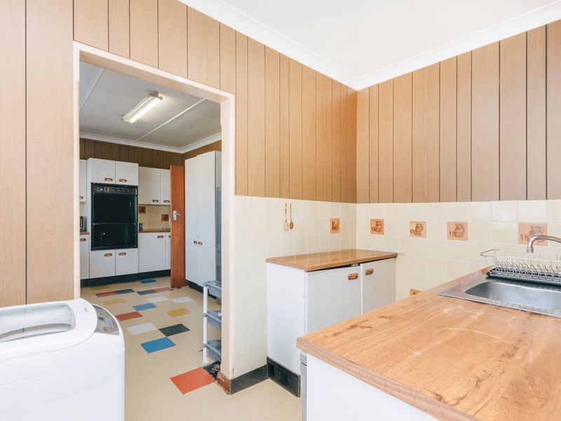 A functional scullery area featuring built-in cabinetry, a stainless steel sink, and tiled splashbacks, with an adjacent kitchen visible through the doorway.