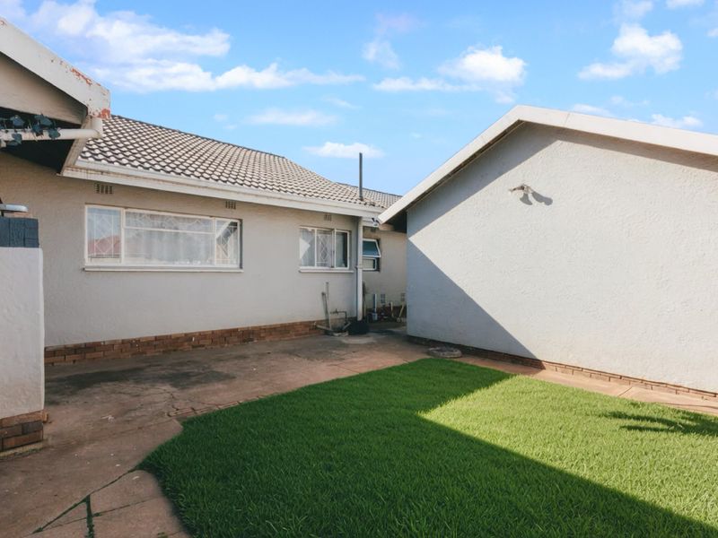A rear exterior view of the property featuring a paved courtyard area, a small lawn, and tiled roof structures.