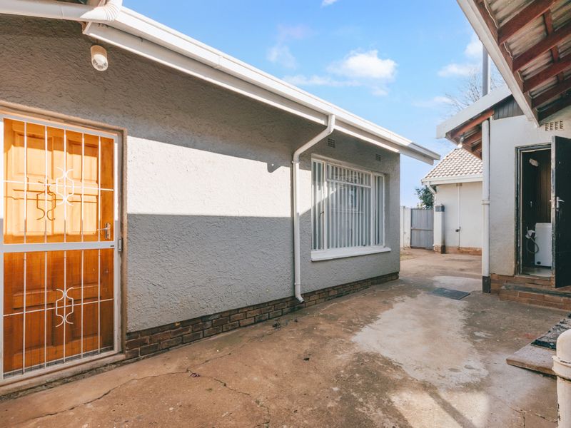 Rear exterior view of the property featuring concrete paving, security gates, and security bars on the windows.