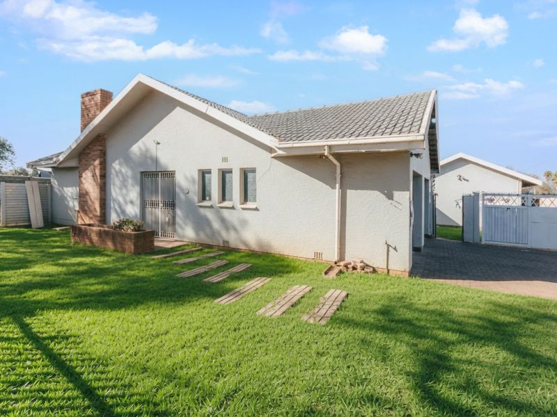 Rear view of the house featuring a tiled roof, brick chimney, paved driveway, and a well-maintained lawn area.