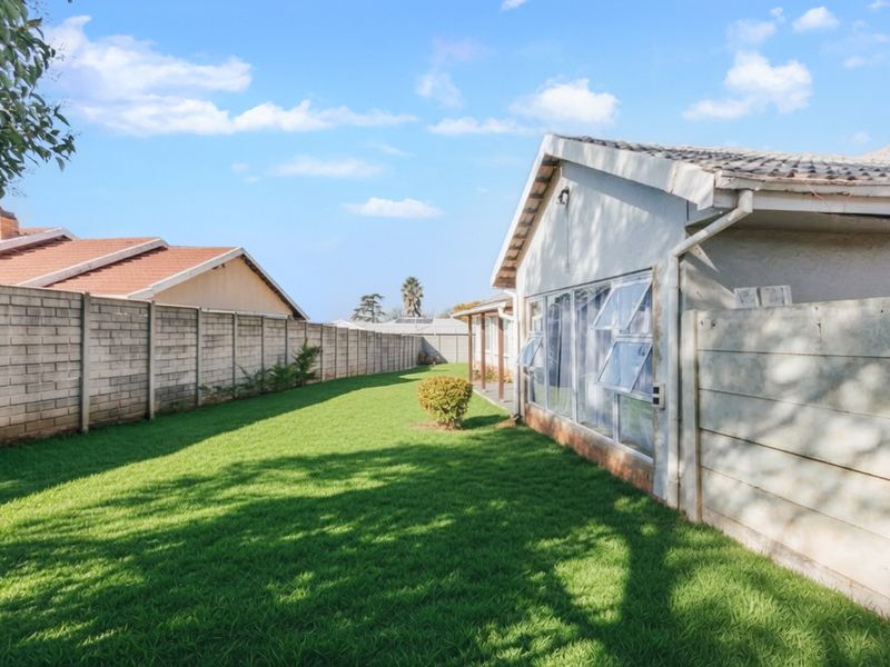 A view of the rear garden featuring a well-maintained lawn, concrete block boundary walls, and the rear elevation of the house with tiled roofing.