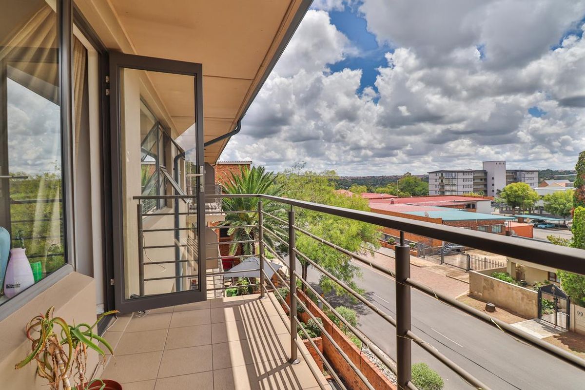 A well-maintained balcony featuring tiled flooring and a metal balustrade, offering an elevated view of the surrounding neighborhood and street.